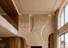 Interior Design Trends 2026: The New Language of Luxury Luxury double-height living room featuring sculptural stone walls, curved cream sofas, warm wood detailing and floor-to-ceiling windows.